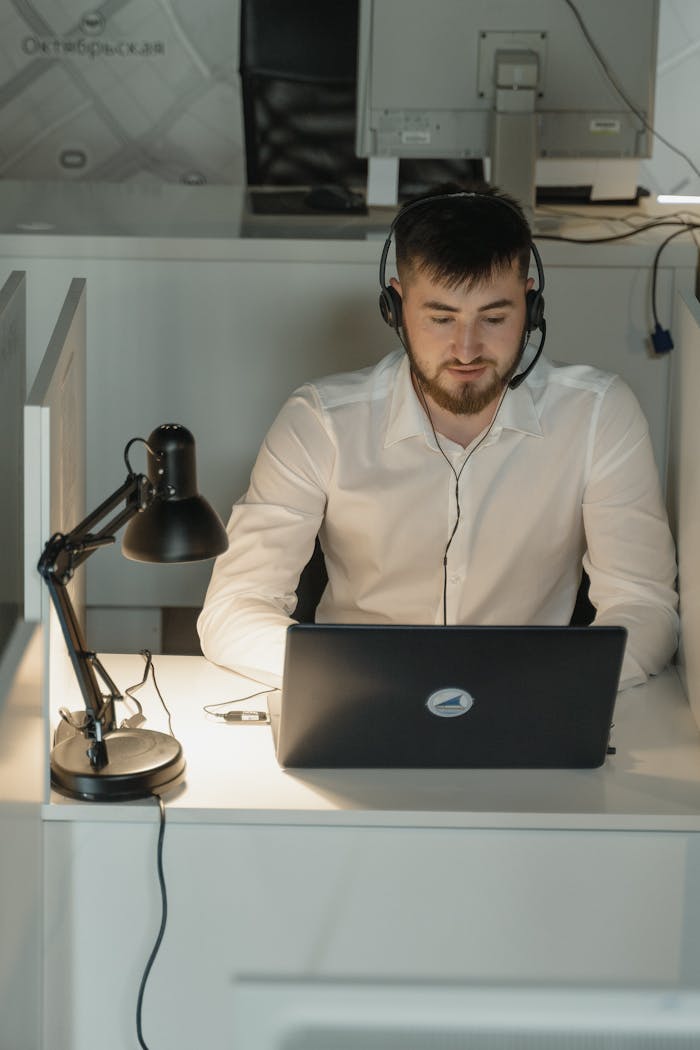 our-services-1 Young professional wearing a headset working on a laptop in a modern office setting.