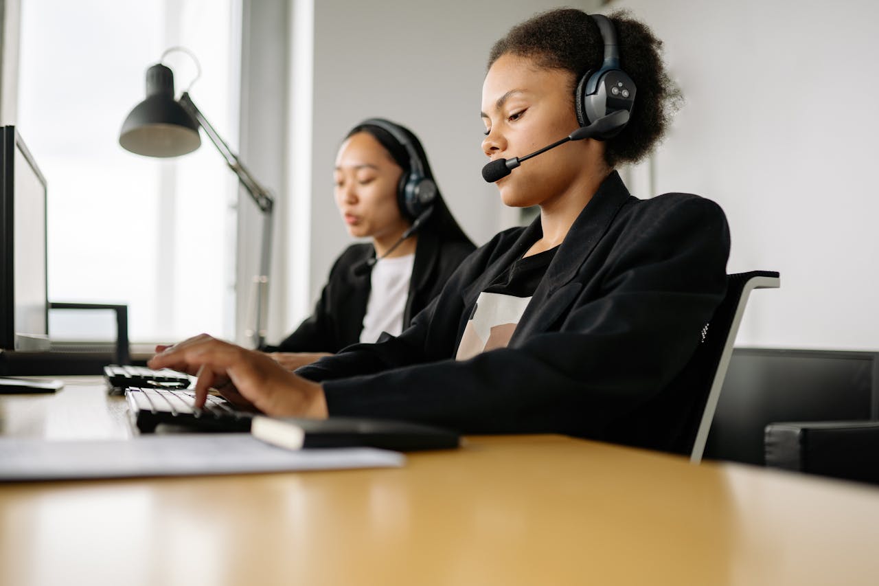 Two call center agents working at desks in an office setting with headsets.